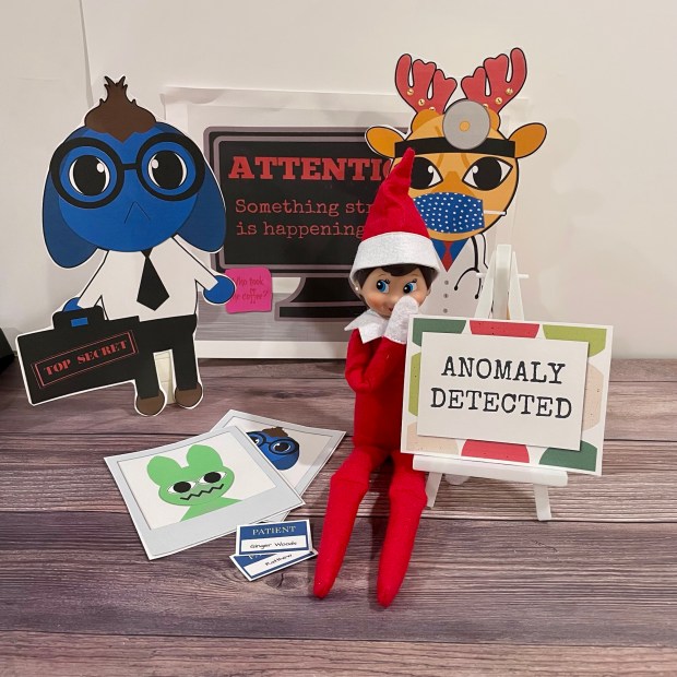Halarious Elf on the shelf idea for fans of the Animal Hospital video game on Roblox. The Elf sits with cartoon animal cutouts (one holding a trop secret brief case), patient id cards, and a sign reading "Anomaly Detected."
